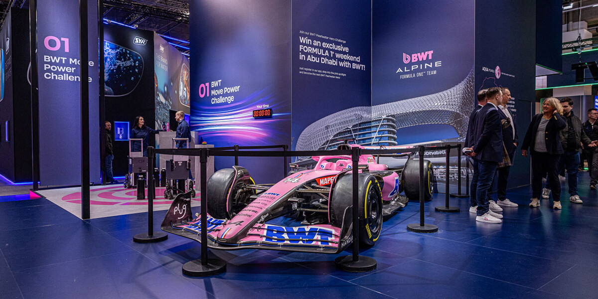 A striking BWT Alpine Formula 1 car showcased at a modern exhibition booth, featuring vibrant pink and blue branding.