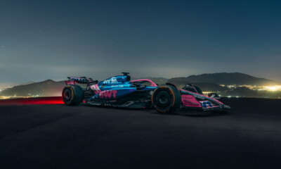 A sleek Formula 1 race car featuring dynamic blue and pink livery is driving on an road at night.