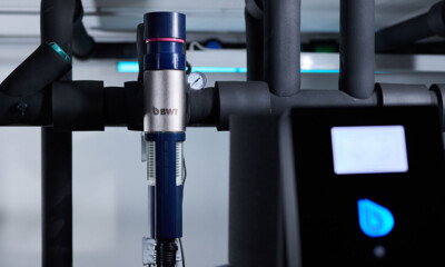 Close-up view of a modern BWT-branded water filtration unit integrated into a network of black pipes. 