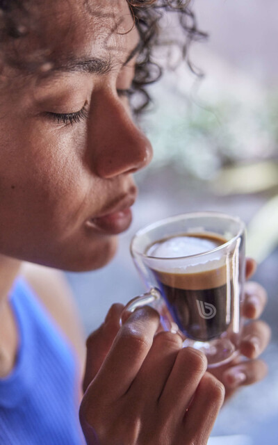 A woman holds a glass espresso cup with the BWT logo and enjoys the aromatic scent of fresh coffee. 