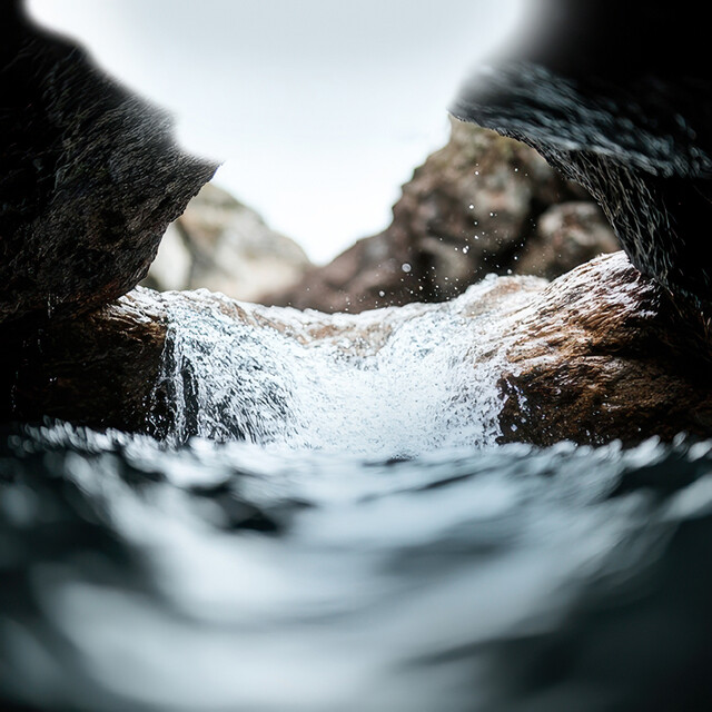 Sparkling, crystal-clear water flows dynamically between rugged rocks in a natural mountain landscape. 
